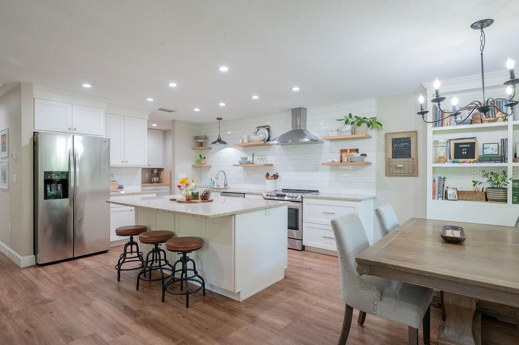 A modern kitchen features white cabinetry, a central island with bar stools, and wood flooring — 216 18TH STREET E, BRADENTON, FL