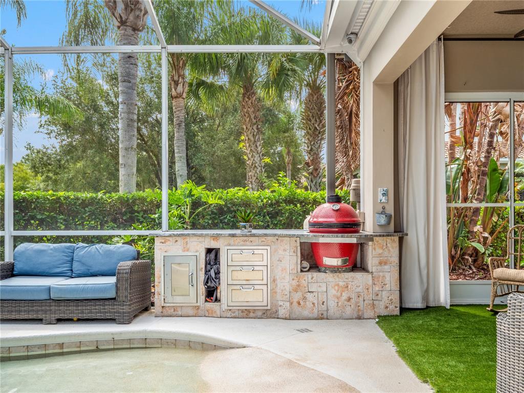 An outdoor kitchen with a red kamado grill sits on a patio beside a pool — 11800 ZELKOVA LANE, ORLANDO, FL