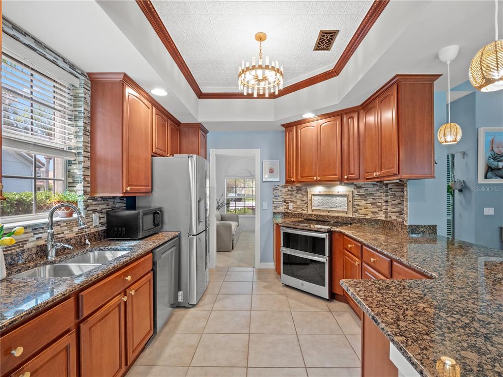 A kitchen features wood cabinets, granite countertops, stainless steel appliances, and a tray ceiling — 11800 ZELKOVA LANE, ORLANDO, FL