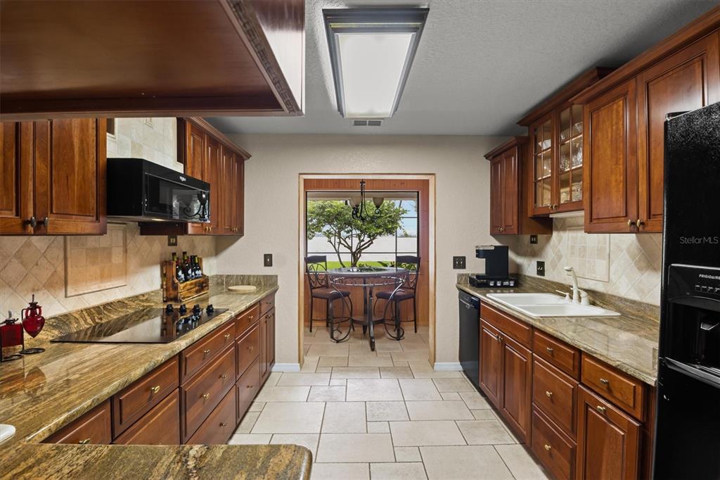 A kitchen with wood cabinets, granite countertops, tile flooring, and a view of a dining area — 926 VAN DRIVE, AUBURNDALE, FL