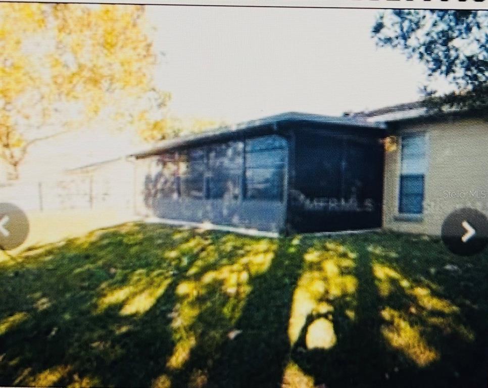 A rear view of a house featuring a screened-in porch and a grassy backyard — 282 SEAL STREET, KISSIMMEE, FL