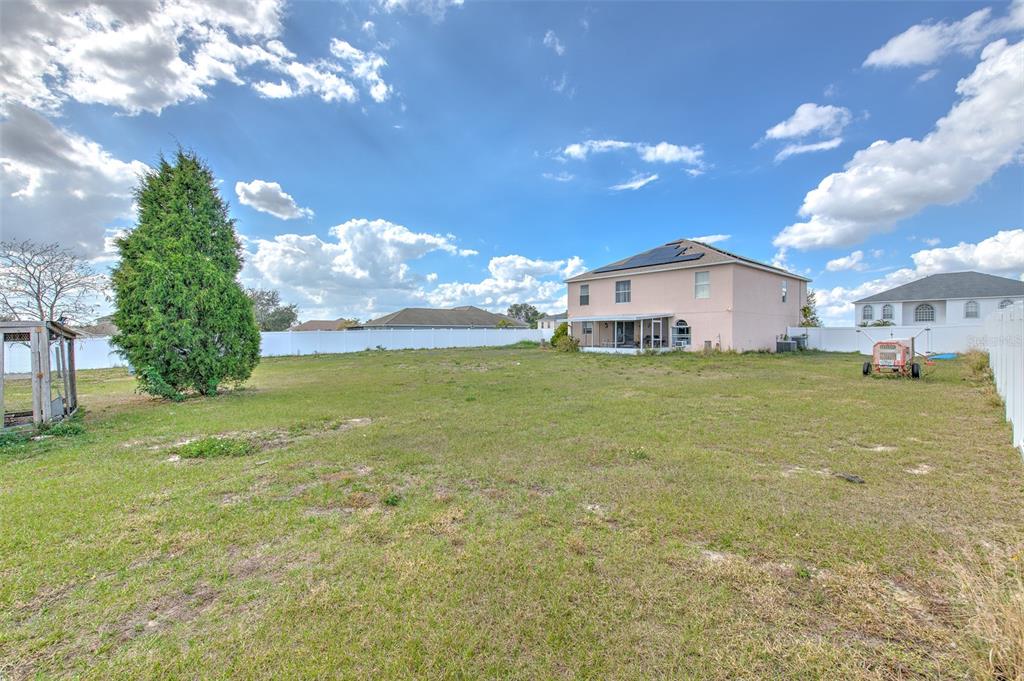 A large, grassy backyard features a tall evergreen tree and a two-story house with solar panels — 169 VISTA VIEW AVENUE, EAGLE LAKE, FL
