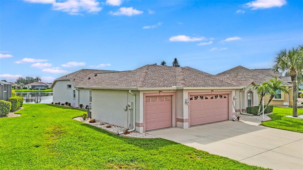 A single-story house with a two-car garage and a concrete driveway sits near a pond — 5494 SABAL TRACE DRIVE, NORTH PORT, FL