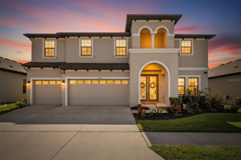 A two-story suburban house with a three-car garage and an arched entryway at dusk — 12444 HORSESHOE BEND DRIVE, LITHIA, FL