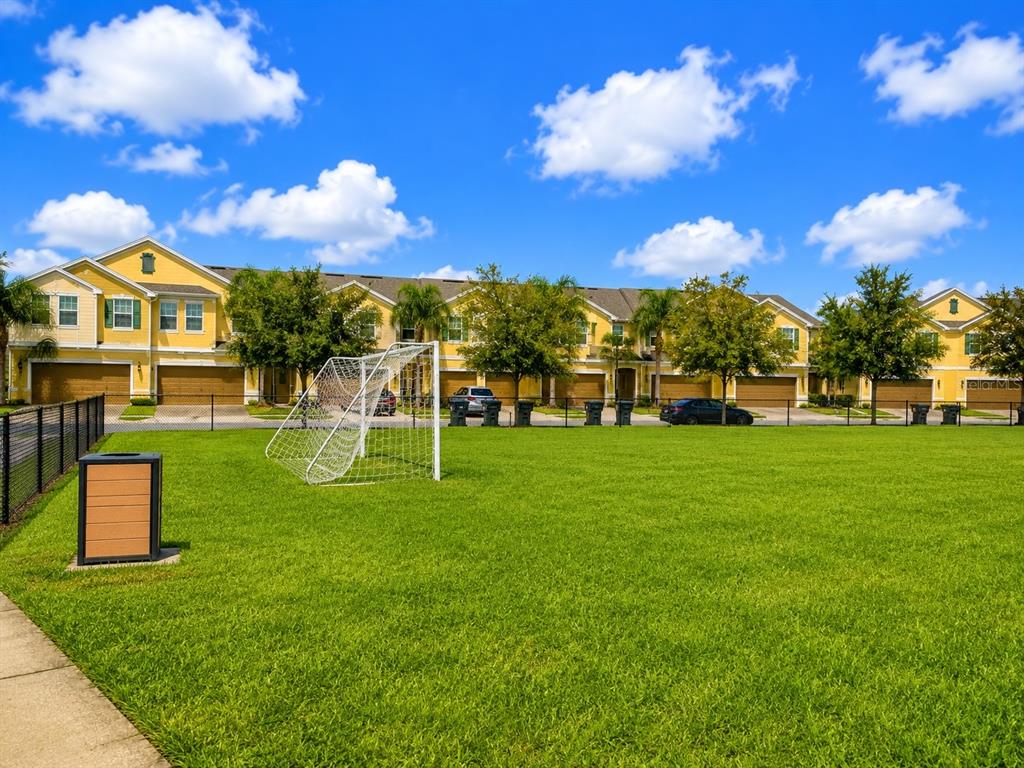 A soccer goal sits on a grassy field in front of a row of yellow townhomes — 9174 TECUMSEH DRIVE, ORLANDO, FL