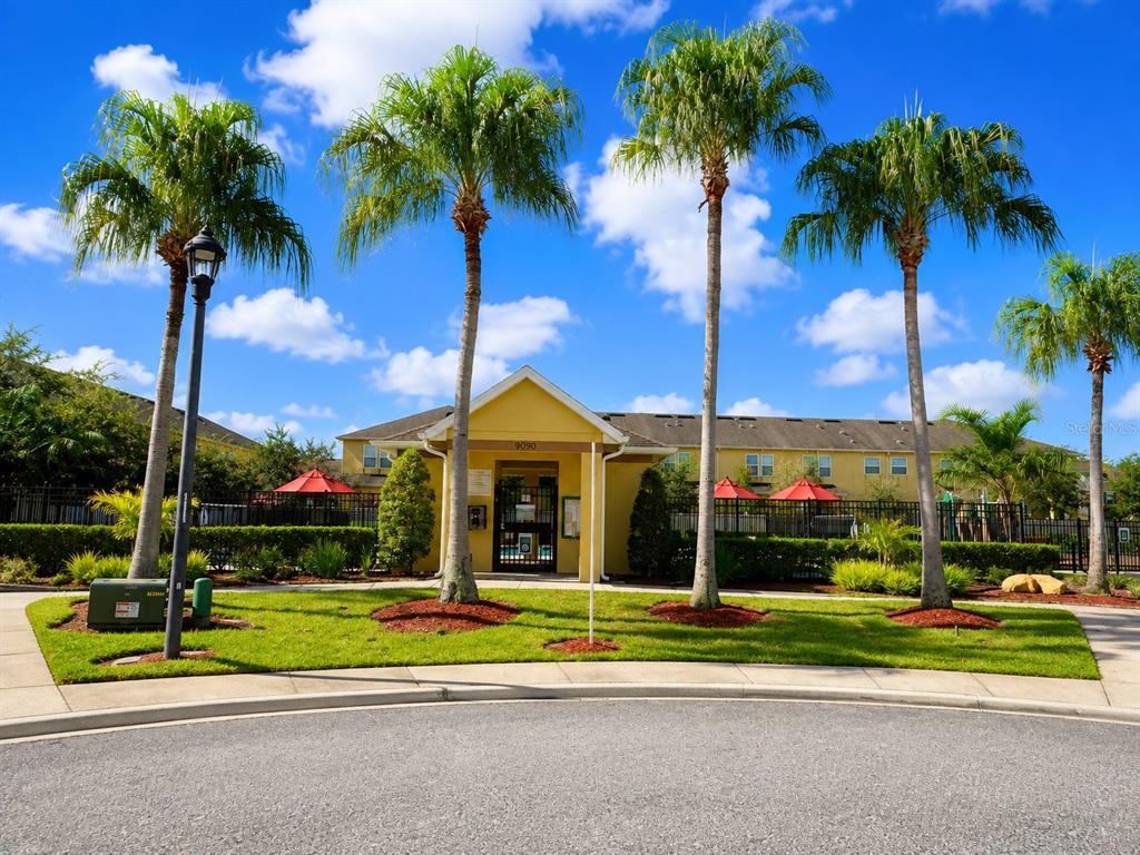 A yellow building with a gated entrance stands behind palm trees under a blue sky — 9174 TECUMSEH DRIVE, ORLANDO, FL