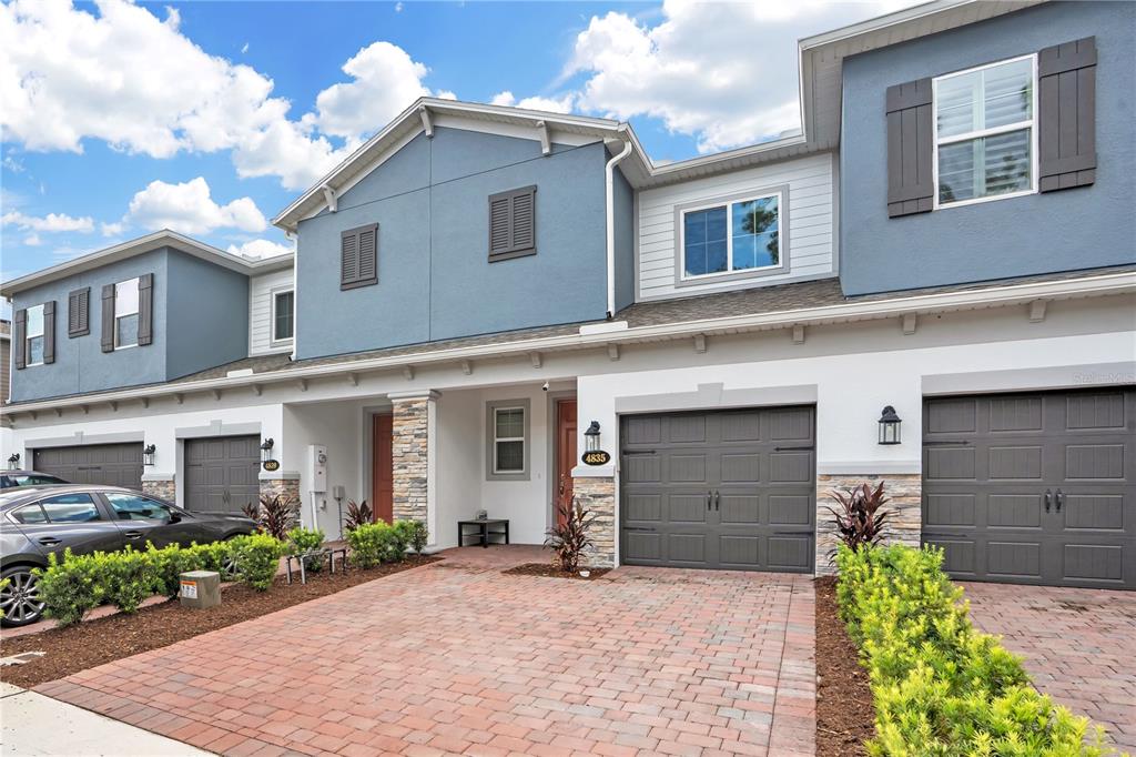 A two-story townhouse exterior features a brick paver driveway, garage doors, and blue siding — 4835 JACKSTAFF WAY, OVIEDO, FL