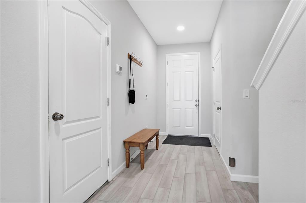 A bright entryway features light wood-look flooring, a wooden bench, and a white front door — 4835 JACKSTAFF WAY, OVIEDO, FL