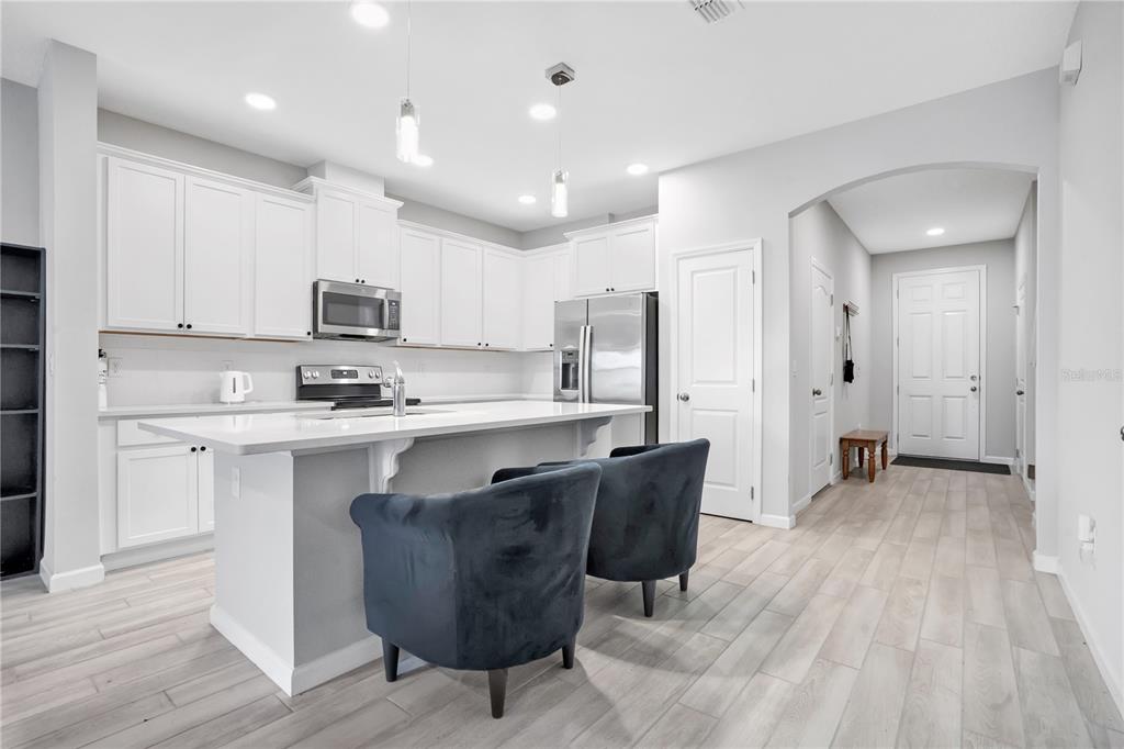 A modern kitchen features white cabinetry, a central island with dark chairs, and light flooring — 4835 JACKSTAFF WAY, OVIEDO, FL