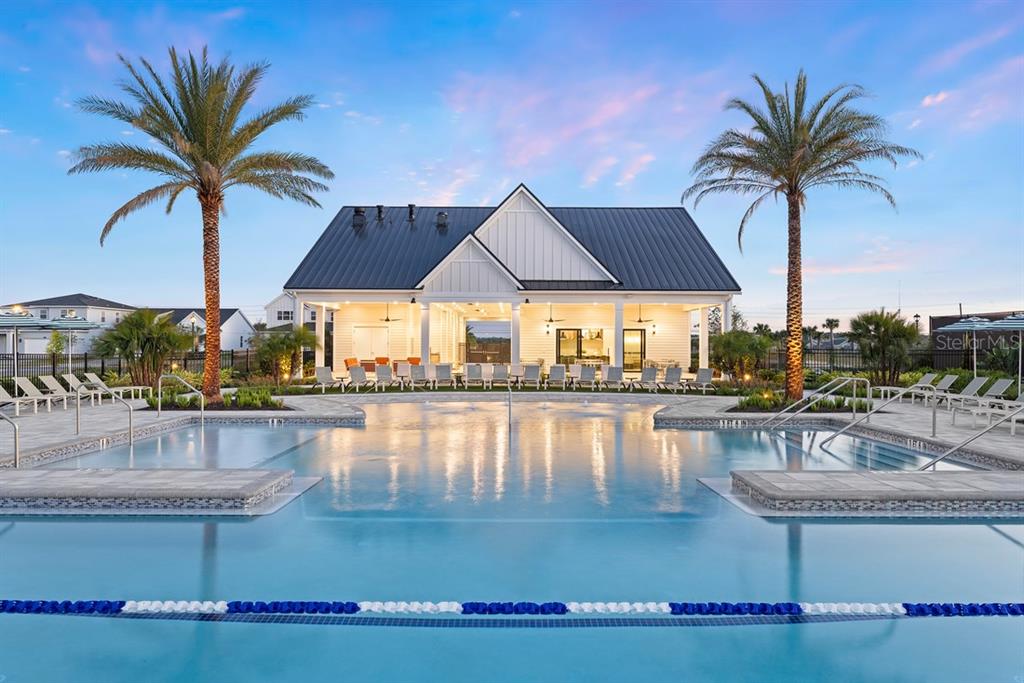 A swimming pool with lounge chairs sits in front of a modern clubhouse at sunset — 1585 STONECLIFF DRIVE, APOPKA, FL