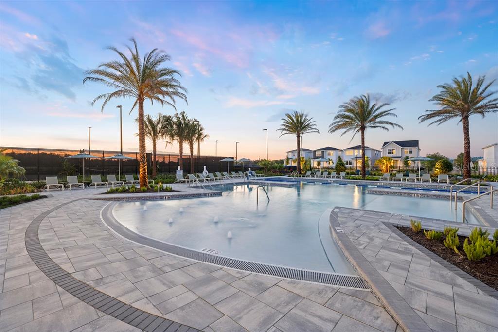A swimming pool with a shallow entry and fountains is surrounded by palm trees and pavers — 1585 STONECLIFF DRIVE, APOPKA, FL