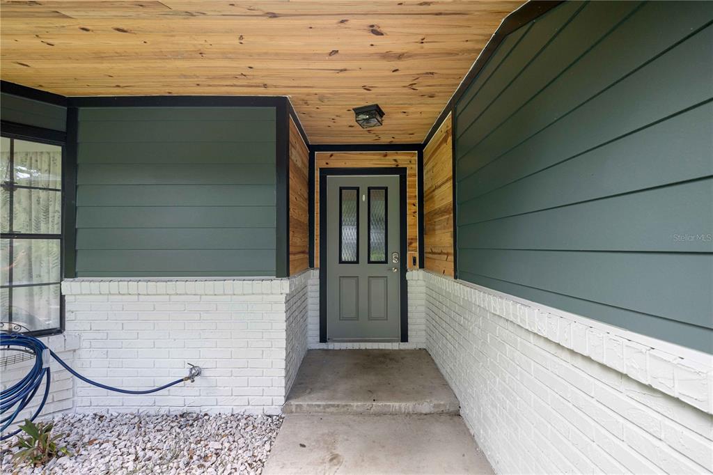 A front entryway features a gray door, white brick base, and green horizontal siding — 6000 SW 109TH PLACE, OCALA, FL
