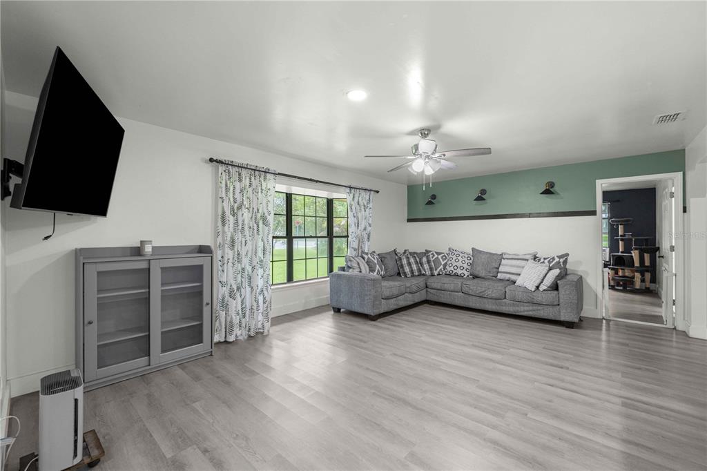 A living room features light wood-look flooring, a gray sectional sofa, and a teal accent wall — 6000 SW 109TH PLACE, OCALA, FL