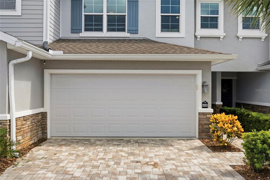 A two-story house exterior features a white garage door, stone accents, and a paved driveway — 5353 RIVERWALK PRESERVE DRIVE, NEW PORT RICHEY, FL