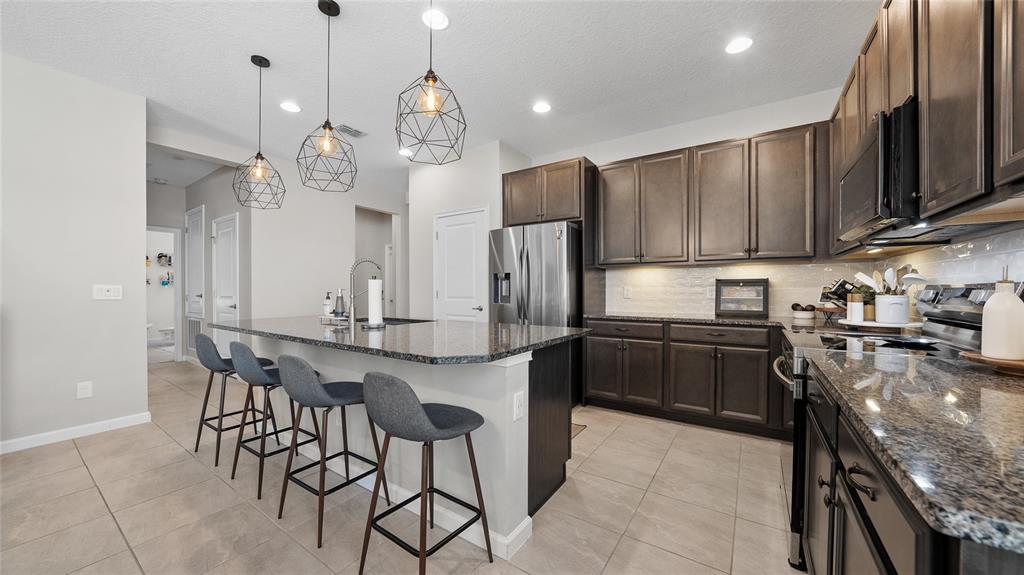 A kitchen features dark wood cabinets, granite countertops, a breakfast bar, and pendant lighting — 891 JETWAY STREET, ORANGE CITY, FL