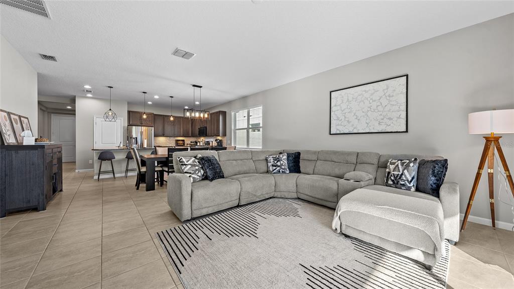 A living room with a gray sectional sofa, a patterned rug, and an open kitchen — 891 JETWAY STREET, ORANGE CITY, FL