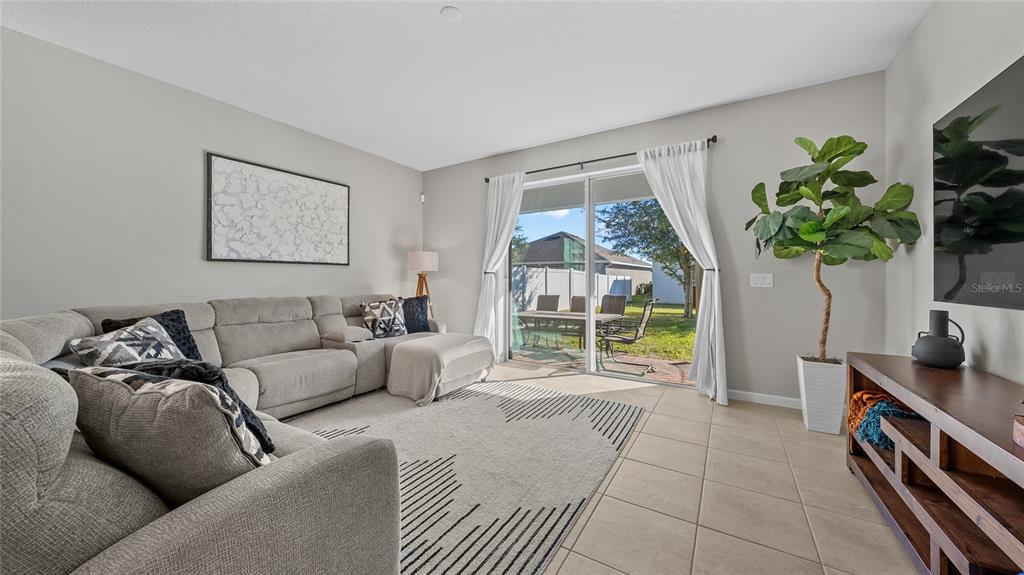 A living room features a gray sectional sofa, a patterned rug, and sliding glass doors — 891 JETWAY STREET, ORANGE CITY, FL
