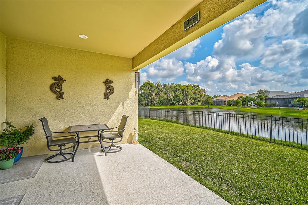 A covered patio with outdoor furniture overlooks a grassy lawn and a lake — 5514 69TH PLACE E, ELLENTON, FL