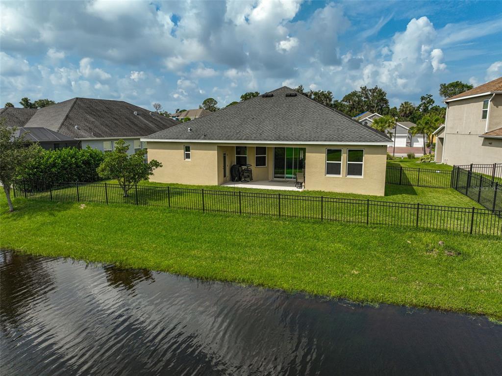 The rear exterior of a tan house with a dark roof overlooks a small pond — 5514 69TH PLACE E, ELLENTON, FL