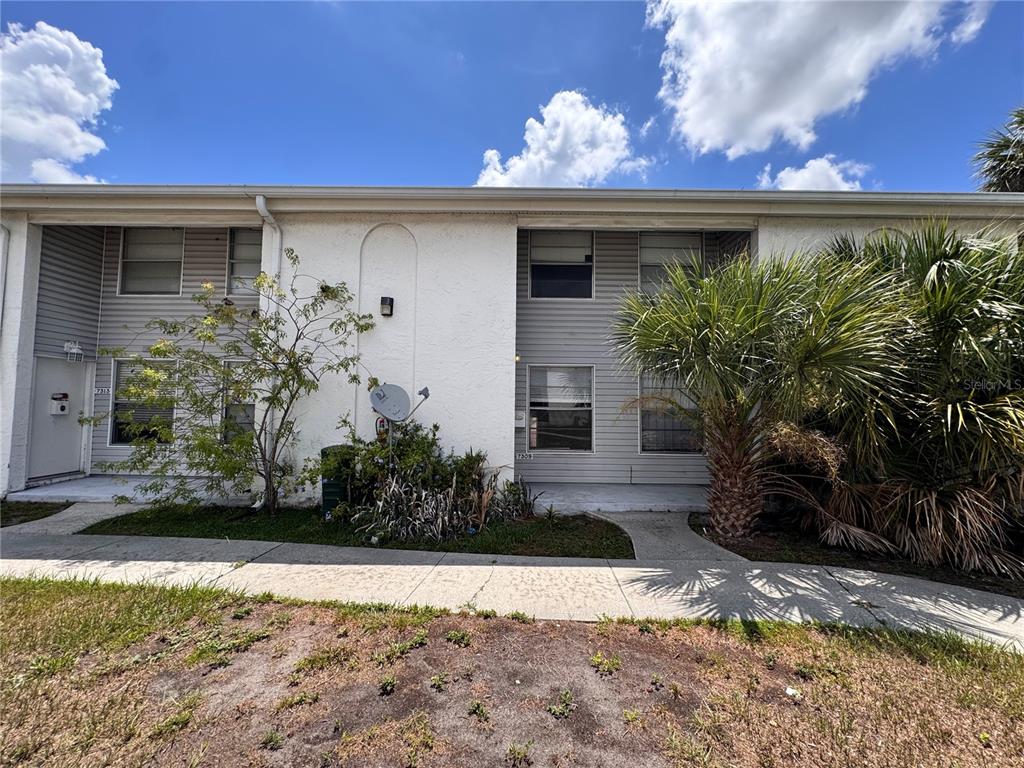 A two-story residential building exterior with gray siding, white stucco, and a palm tree — 7309 JACKSON SPRINGS ROAD UNIT 7309, TAMPA, FL