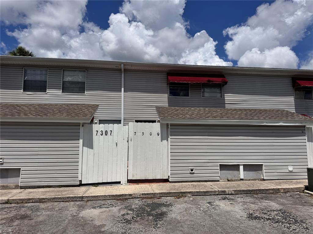 The exterior of a two-story townhouse features gray siding, white privacy gates, and red awnings — 7309 JACKSON SPRINGS ROAD UNIT 7309, TAMPA, FL