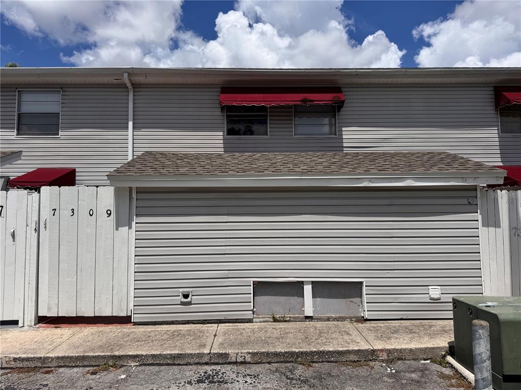 The exterior of a two-story townhouse features gray horizontal siding and red window awnings — 7309 JACKSON SPRINGS ROAD UNIT 7309, TAMPA, FL