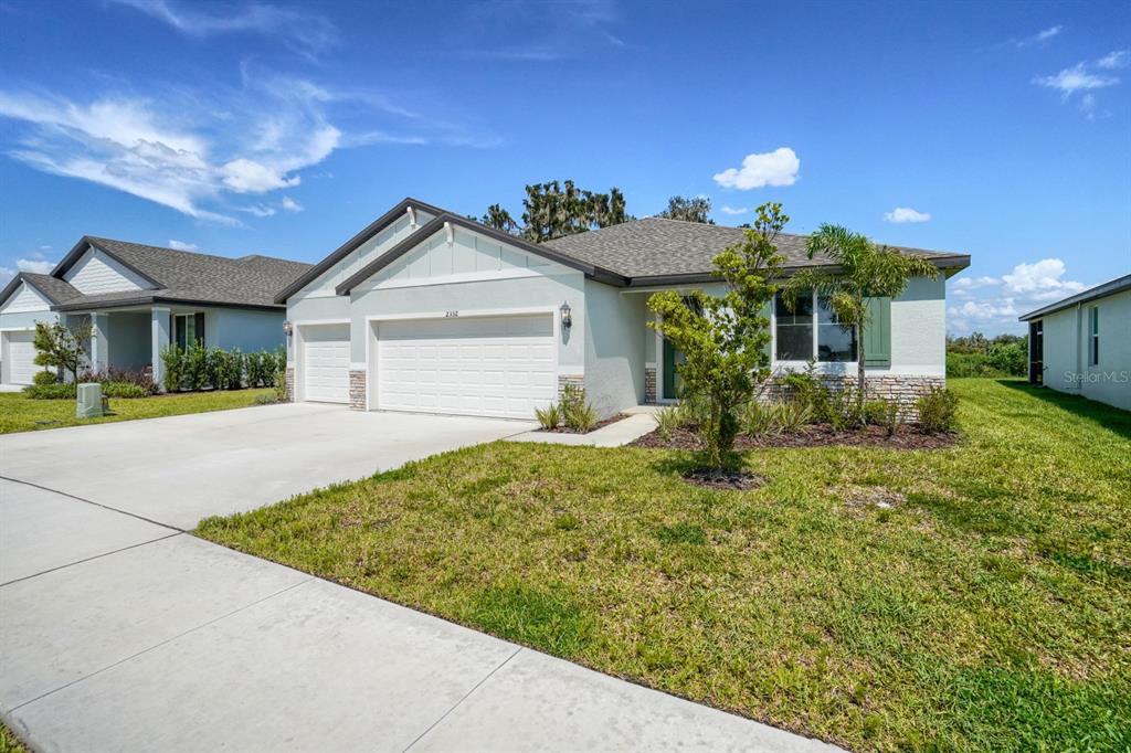 A light-colored single-story house with a three-car garage and a concrete driveway — 2332 CITRUS BLOOM DRIVE, BARTOW, FL
