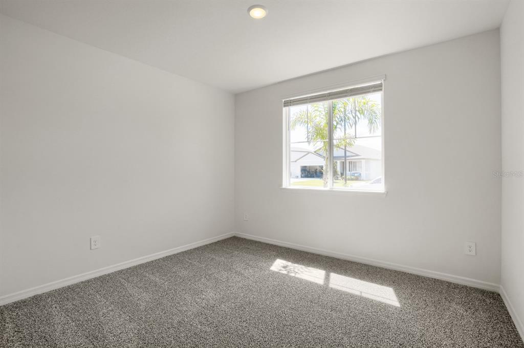 An empty bedroom features gray carpet, white walls, and a single window with blinds — 2332 CITRUS BLOOM DRIVE, BARTOW, FL