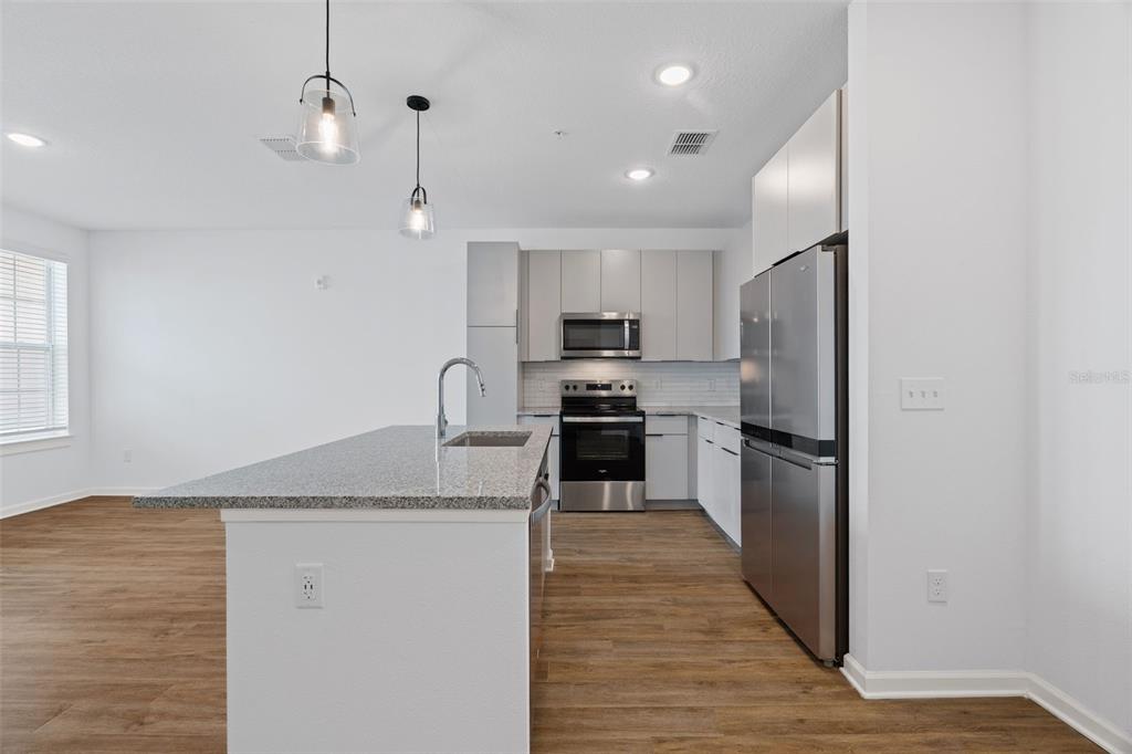 A modern kitchen features a granite-topped island, stainless steel appliances, and light-colored cabinetry — 1700 RANCH ROAD UNIT A4-7306, NOKOMIS, FL