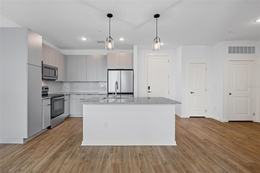 A modern kitchen features light gray cabinetry, stainless steel appliances, and a central granite island — 1700 RANCH ROAD UNIT A4-7306, NOKOMIS, FL