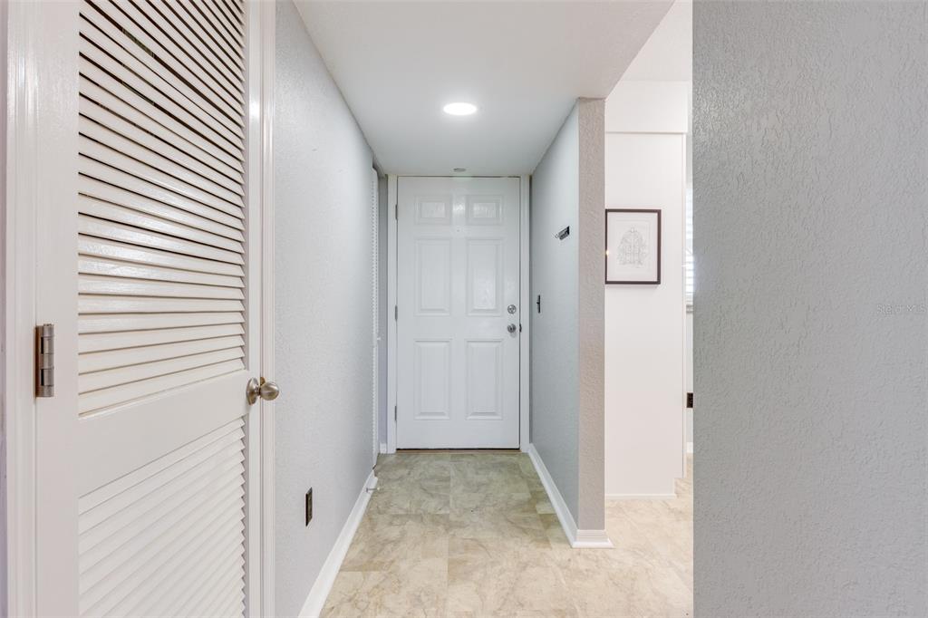 A hallway with light-colored walls, tile flooring, a louvered closet door, and a white entry door — 175 KINGS HIGHWAY UNIT 733, PUNTA GORDA, FL