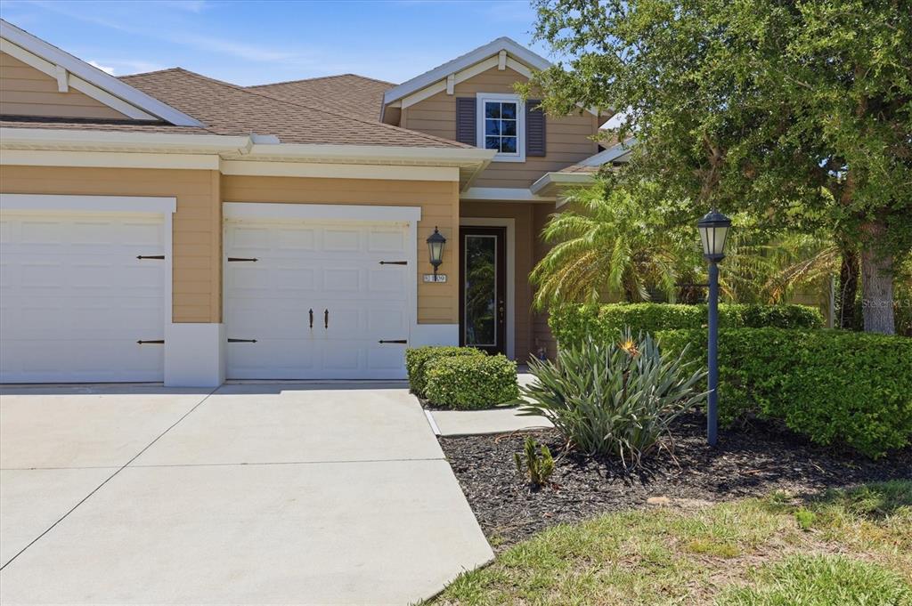 A tan house exterior features a white garage door, a front entrance, and landscaped bushes — 1109 THORNBURY DRIVE, PARRISH, FL