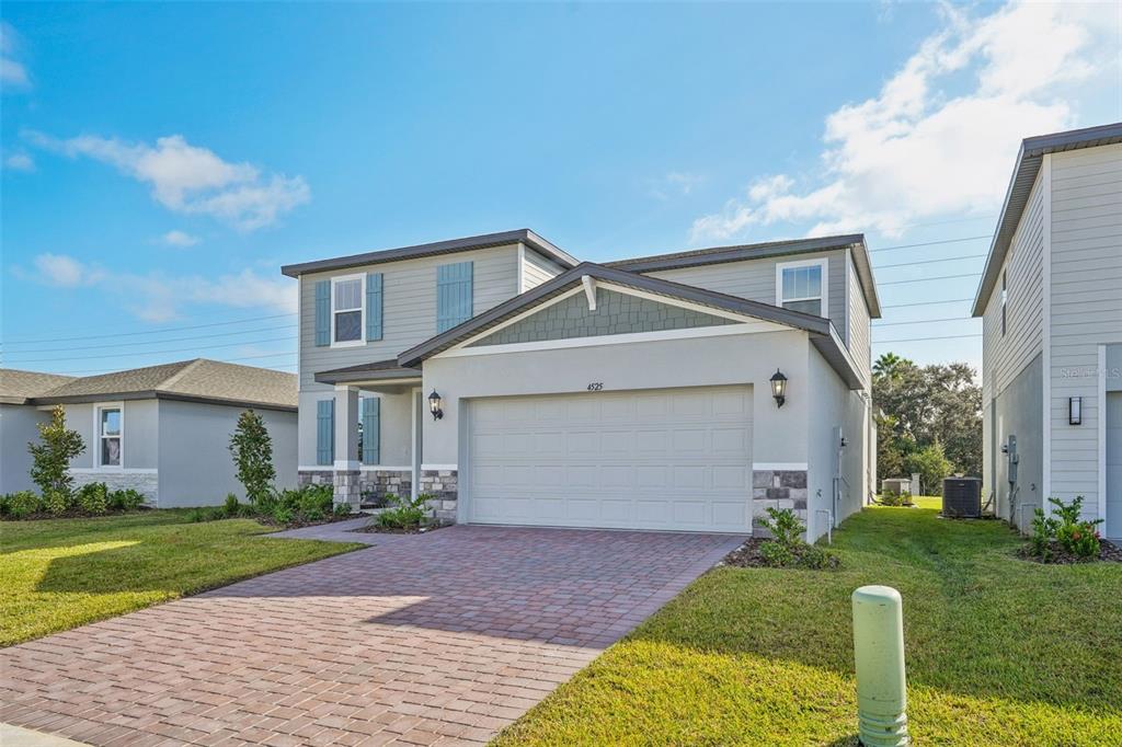 A two-story suburban house with a gray exterior, stone accents, and a paved driveway — 4525 SIDESADDLE TRAIL, ST CLOUD, FL