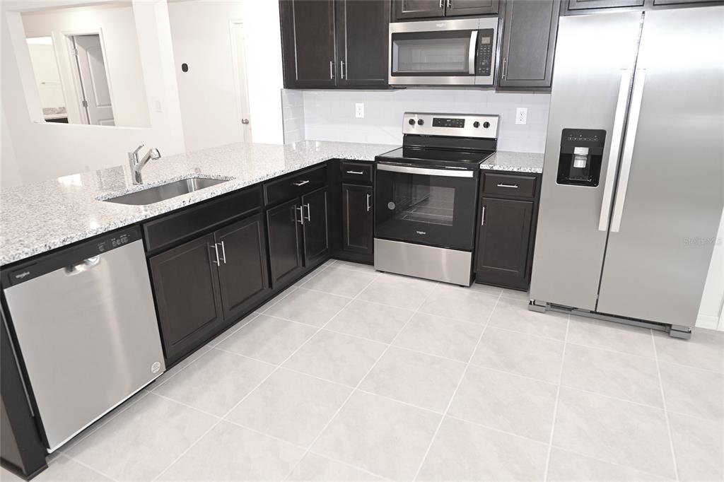 A kitchen features dark wood cabinets, granite countertops, stainless steel appliances, and light tile flooring — 9532 SANDY BLUFFS CIRCLE, PARRISH, FL