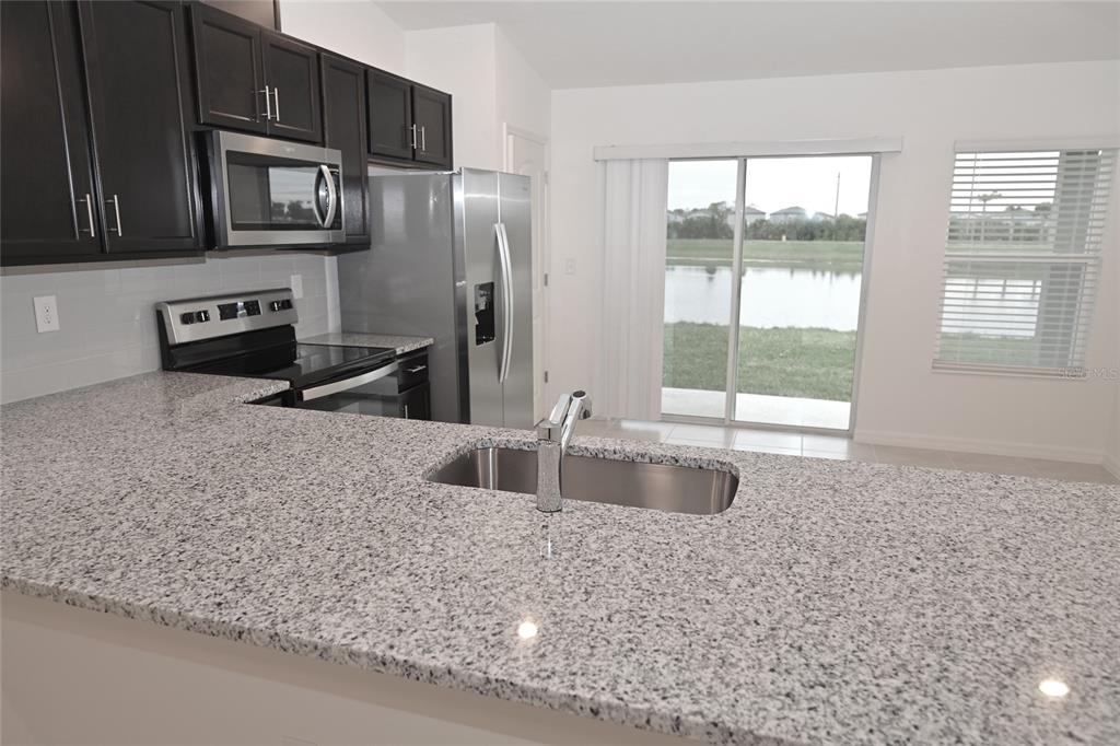 A kitchen features dark cabinets, granite countertops, stainless steel appliances, and a view of water — 9532 SANDY BLUFFS CIRCLE, PARRISH, FL