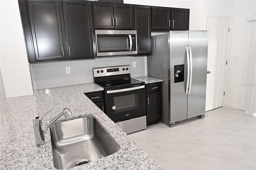 A kitchen features dark cabinets, granite countertops, stainless steel appliances, and a stainless steel sink — 9532 SANDY BLUFFS CIRCLE, PARRISH, FL