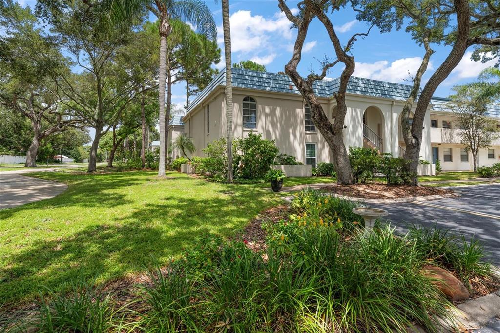 A two-story apartment building with a light-colored exterior and a blue roof sits among trees — 1975 W BAY DRIVE UNIT 109, LARGO, FL