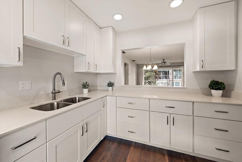 A modern kitchen features white cabinets, light countertops, a double sink, and dark wood flooring — 1975 W BAY DRIVE UNIT 109, LARGO, FL