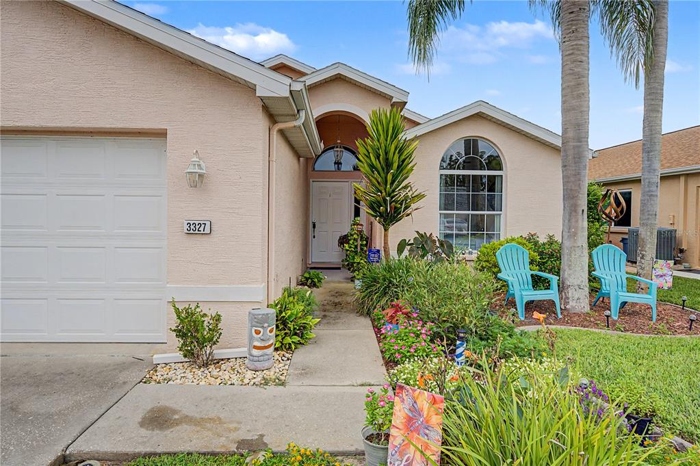 A tan stucco house exterior features a front door, garage, and a landscaped front yard — 3327 SCORECARD DRIVE, NEW PORT RICHEY, FL