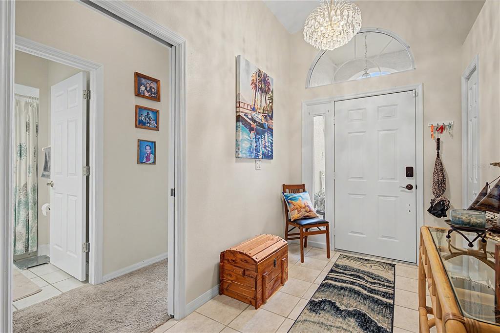 An entryway features a white front door, a wooden chest, a chair, and tile flooring — 3327 SCORECARD DRIVE, NEW PORT RICHEY, FL