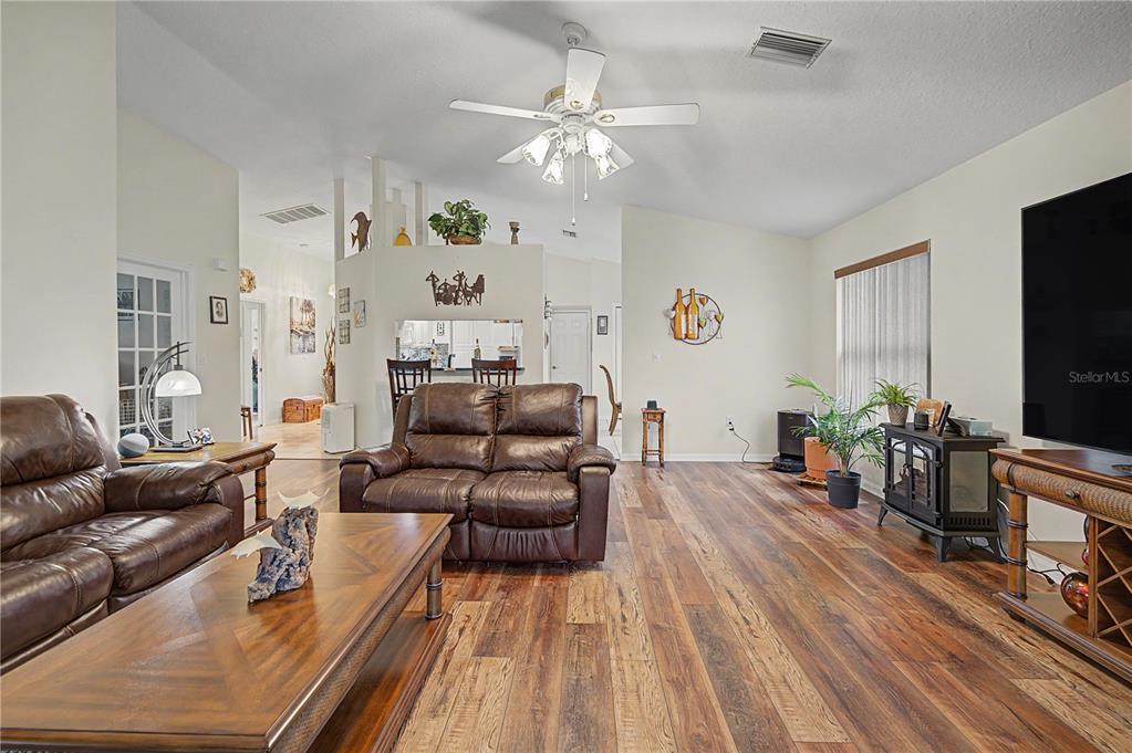 A living room features wood-look flooring, brown leather furniture, and a ceiling fan — 3327 SCORECARD DRIVE, NEW PORT RICHEY, FL