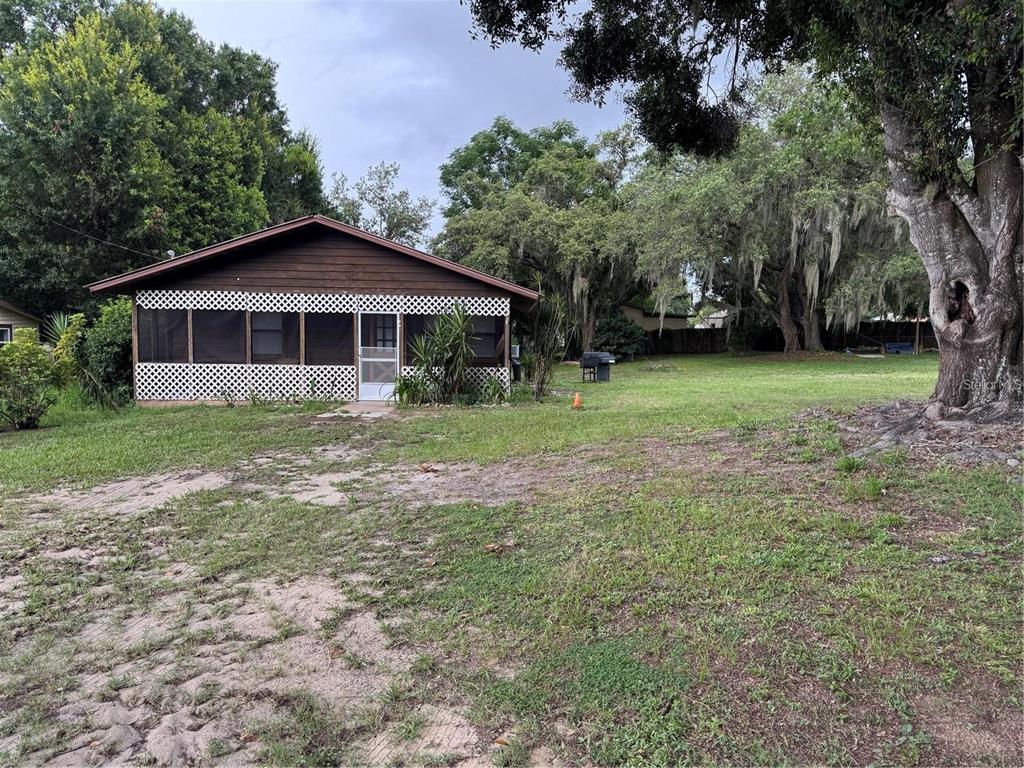A small, brown, single-story house with a screened-in porch sits on a grassy lot — 224 CHESNEY BOULEVARD, FROSTPROOF, FL