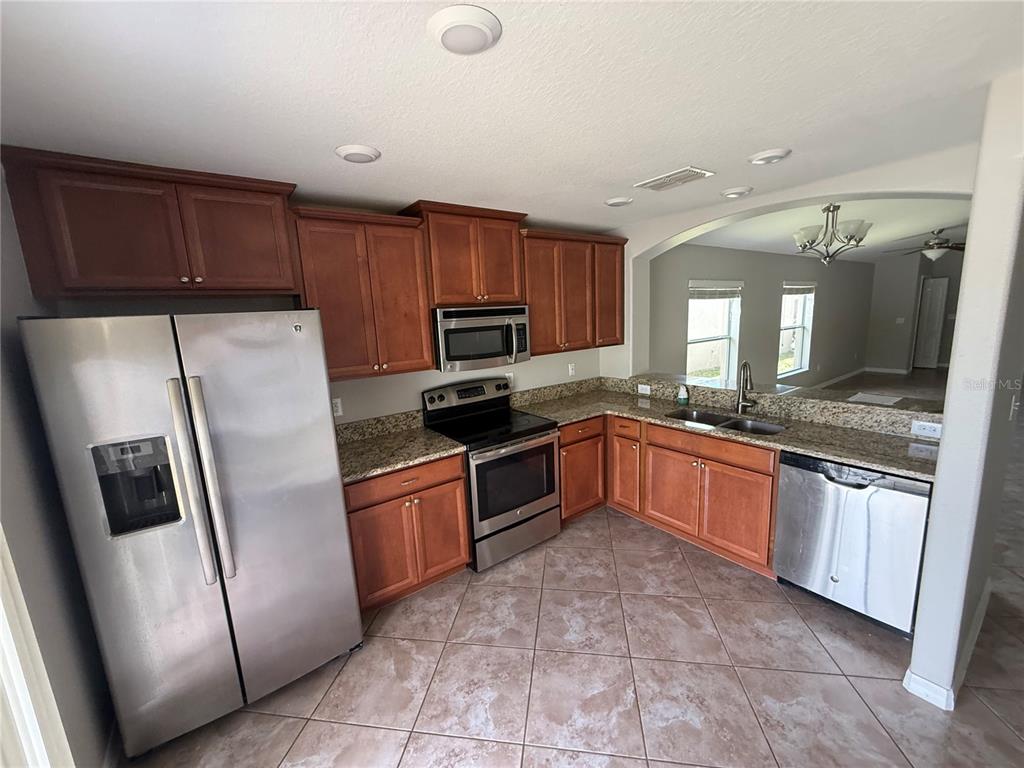 A kitchen features wood cabinets, granite countertops, stainless steel appliances, and tile flooring — 1970 HAWKS VIEW DRIVE, RUSKIN, FL