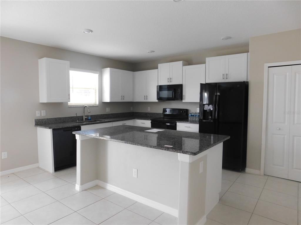 A kitchen features white cabinets, dark granite countertops, black appliances, and a central island — 238 ARGYLL DRIVE, SPRING HILL, FL