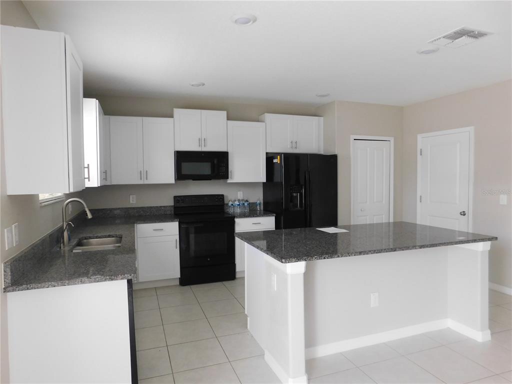A kitchen features white cabinets, black appliances, granite countertops, and a central island — 238 ARGYLL DRIVE, SPRING HILL, FL