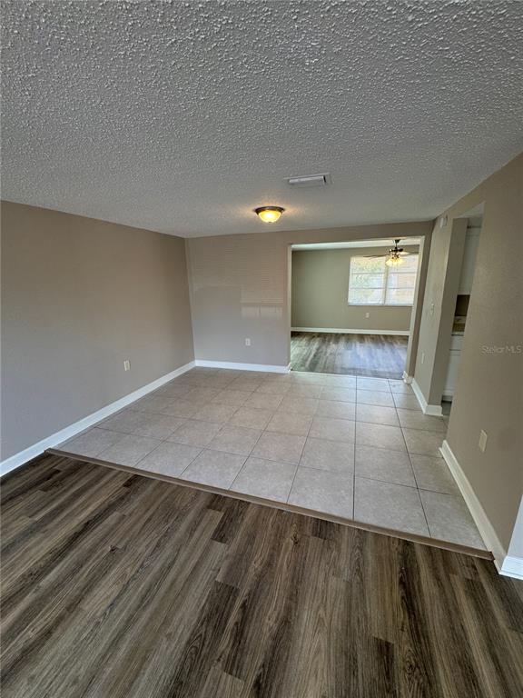 An empty room with wood-look flooring, beige walls, and an adjacent tiled area — 6135 SEABREEZE DRIVE, PORT RICHEY, FL