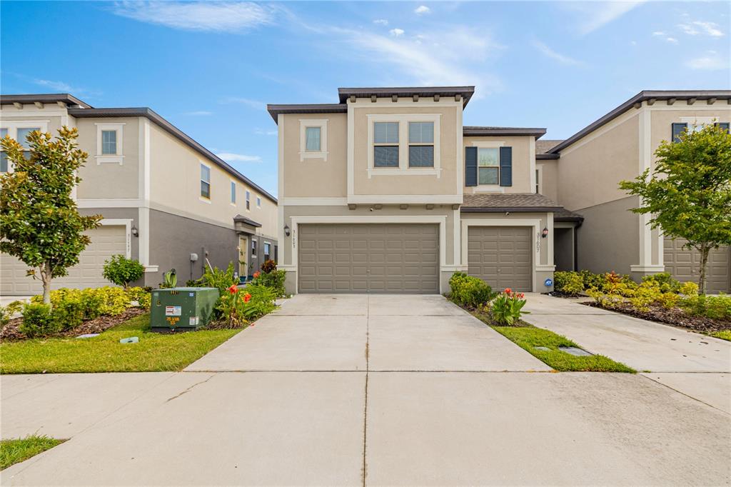 A two-story townhouse with a beige stucco exterior, two garage doors, and a concrete driveway — 31603 BLUE PASSING LOOP, WESLEY CHAPEL, FL