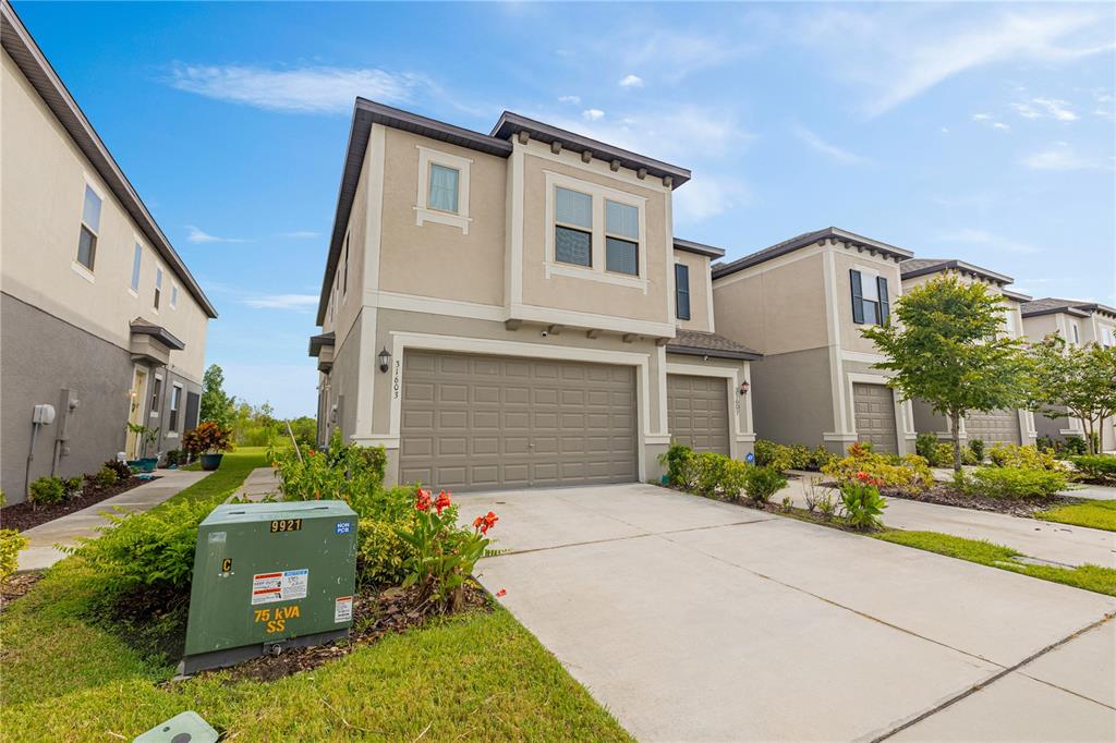 A two-story suburban townhouse with a two-car garage and a green utility box outside — 31603 BLUE PASSING LOOP, WESLEY CHAPEL, FL