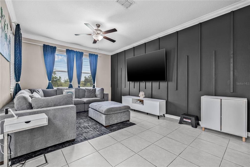 A living room features a gray sectional sofa, a wall-mounted television, and a dark accent wall — 31603 BLUE PASSING LOOP, WESLEY CHAPEL, FL