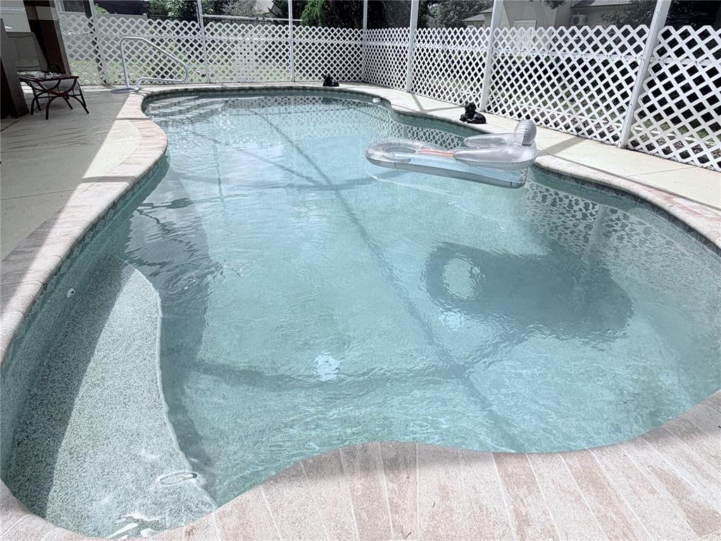 A swimming pool with a floating lounge chair is enclosed by a white lattice screen — 6345 BODMIN LANE, NORTH PORT, FL